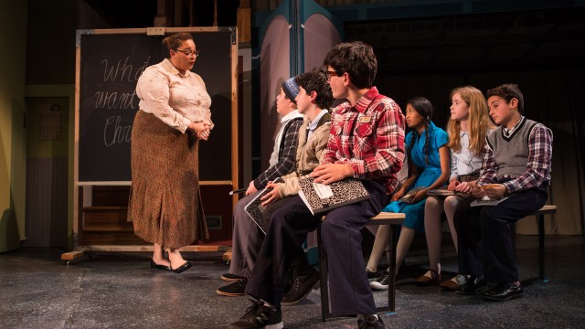 Miss Shields (Katrina Lauren McGraw) collects her students' papers.